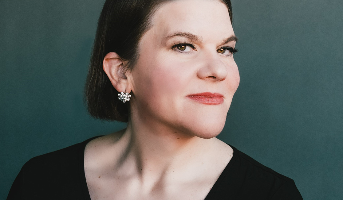 Meredith Arwady is a woman with short, dark hair coming to just below her ears. She is wearing a black top and looks at the camera with a slight smirk.